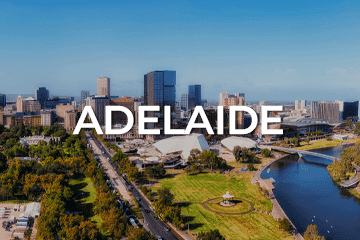 Aerial view of Adelaide city skyline with modern buildings, green parks, and a river under a clear blue sky. Bold white text 'ADELAIDE' is overlaid on the center, capturing the vibrant hub where opportunities like businesses for sale thrive.