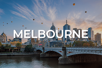 A scenic view of Melbourne's skyline at sunrise, with several hot air balloons in the sky. The Yarra River and a bridge are in the foreground. The word 'Melbourne' is prominently displayed over the image, capturing the city's allure—a perfect spot to consider your next business for sale venture.